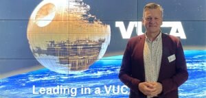 Man voor VUCA-scherm presenteert openingsdia van VUCA@Work web-event