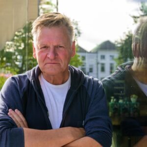 man leunend tegen glazen raam met zijn spiegelbeeld erin